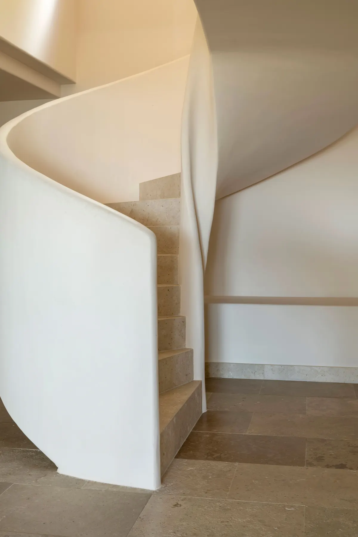 Ca L’Àmfora — a sculpted white staircase curving through a warm plaster hall
