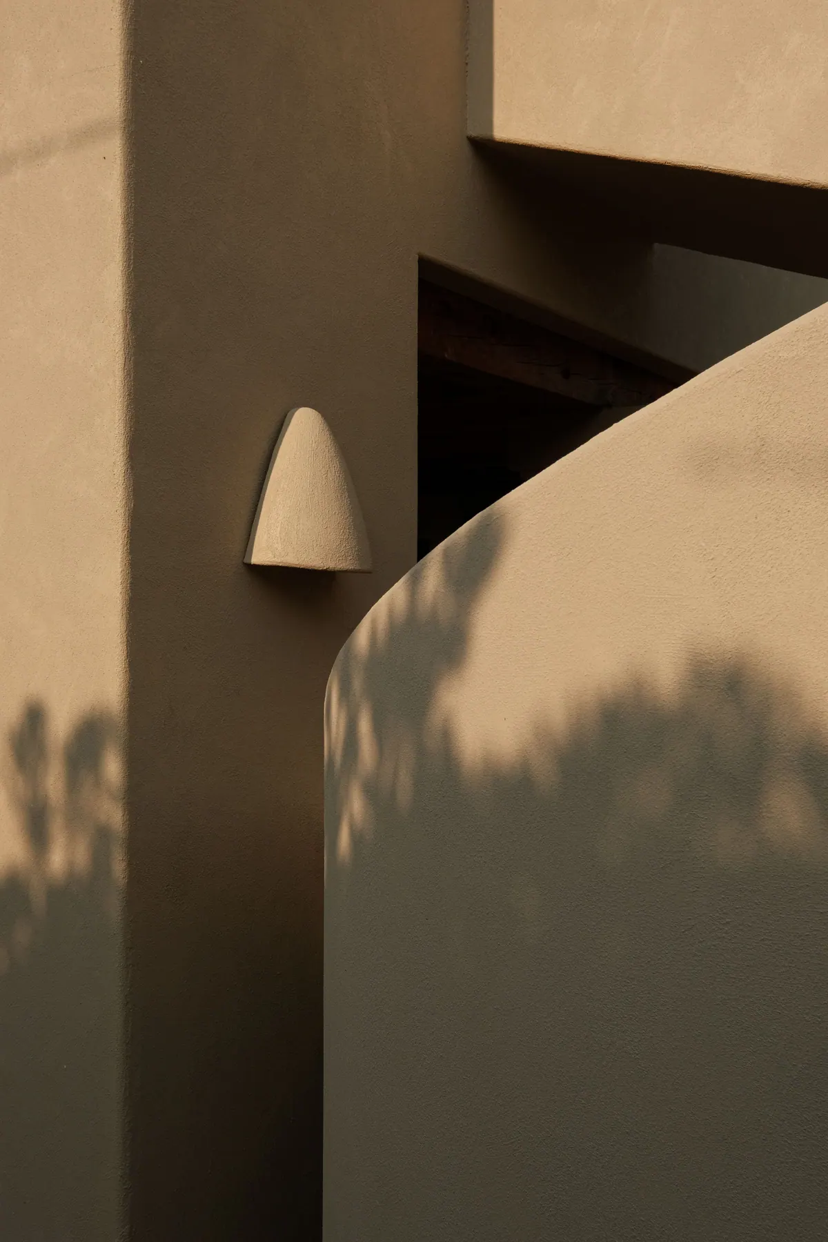 A sculpted wall light on a warm rendered wall, with the shadow of foliage
