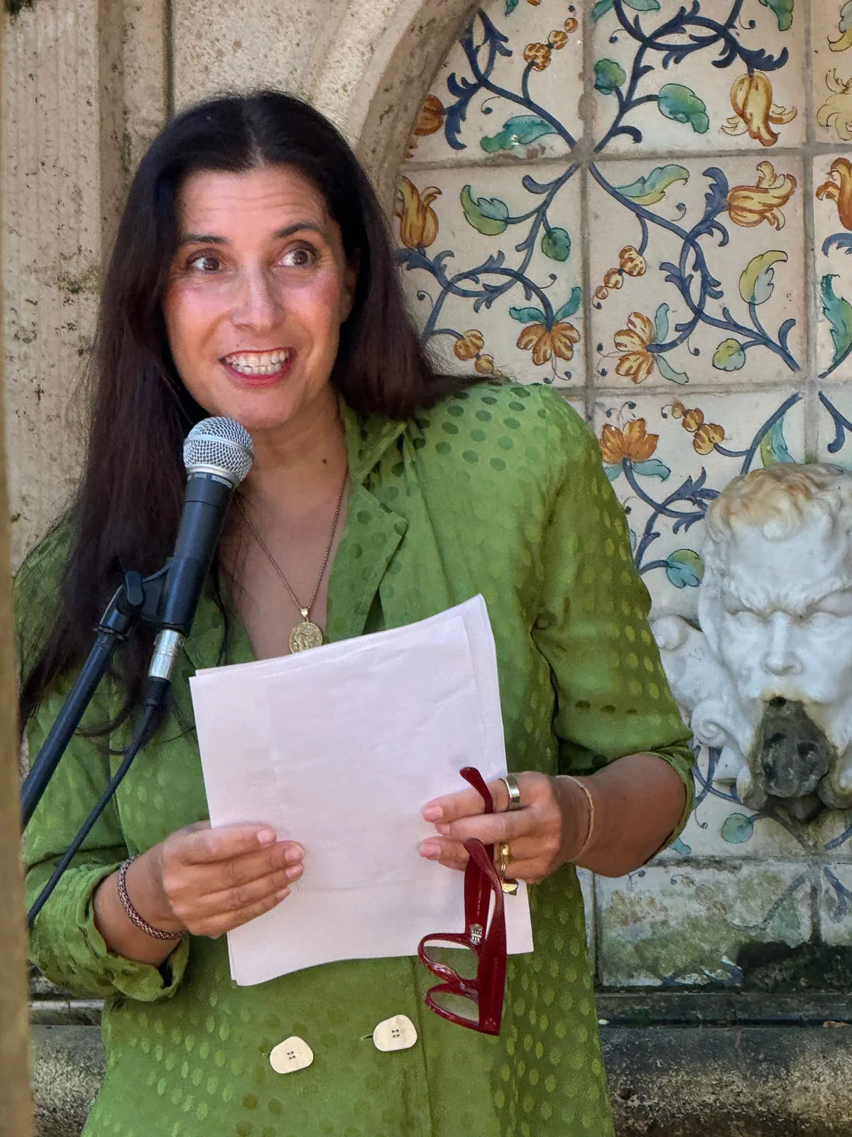 Jessica Bataille speaking at a microphone in front of a painted tile fountain