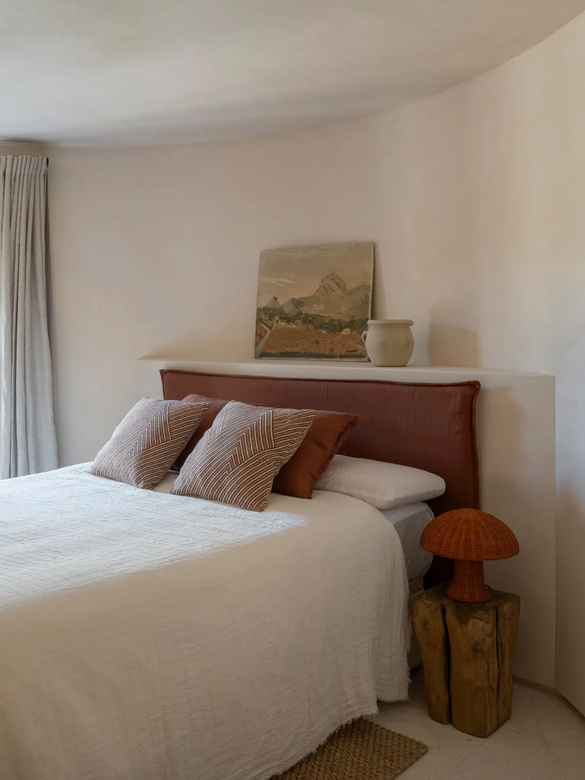 Ca La Mer — a bedroom with a curved lime wall, terracotta linen and a small landscape painting