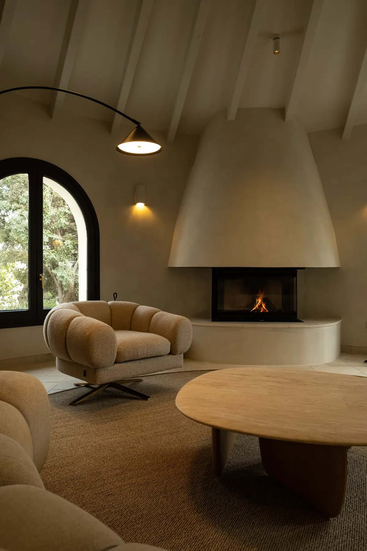 A sculpted plaster fireplace, a rounded armchair and an arched window