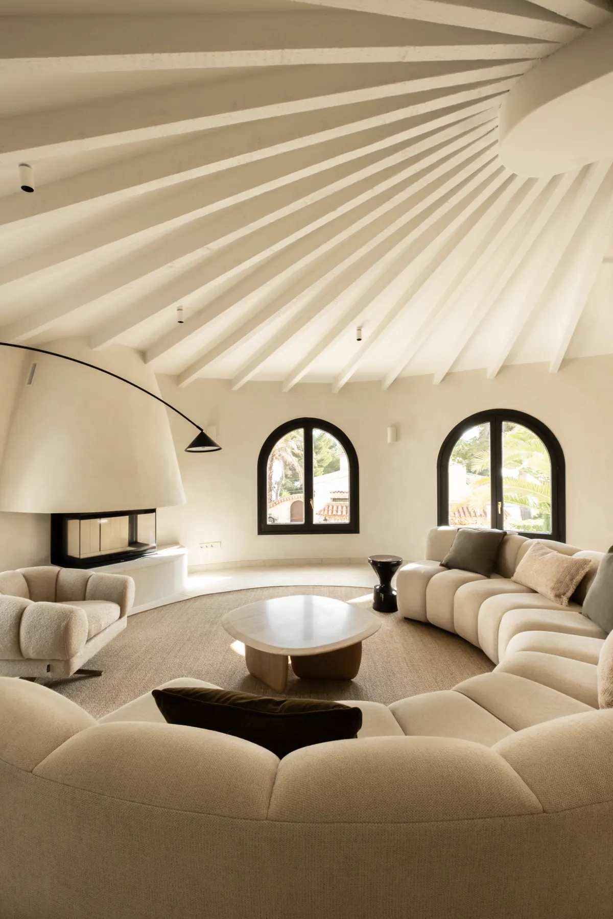 A round lounge beneath radiating white beams, with a curved sofa and arched windows