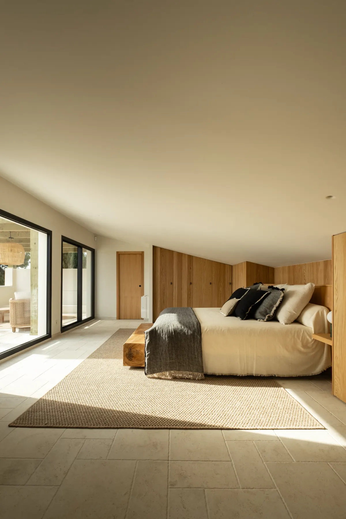 A bedroom with timber wall panelling and wide glazing onto a terrace
