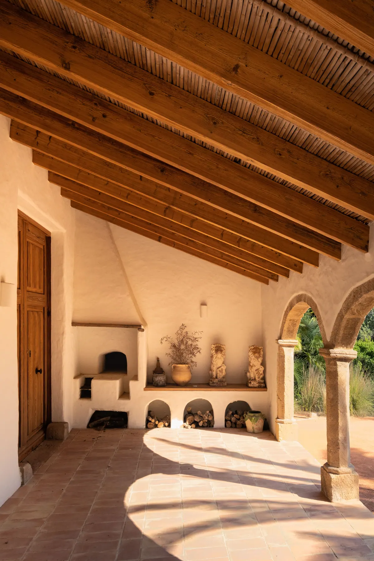 A covered porch with timber beams, terracotta floor and a stone arch