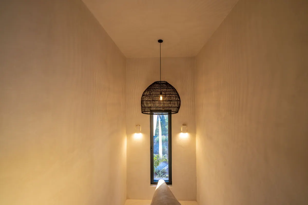 A narrow lime-rendered passage with a woven pendant and a slot window