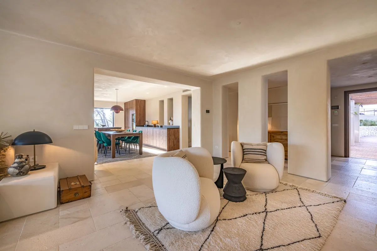 A light living room with curved armchairs, a Berber rug and views into the dining area