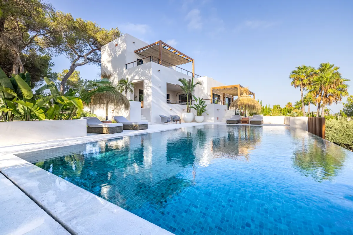 An infinity pool in front of a white Mediterranean villa with palms and terraces