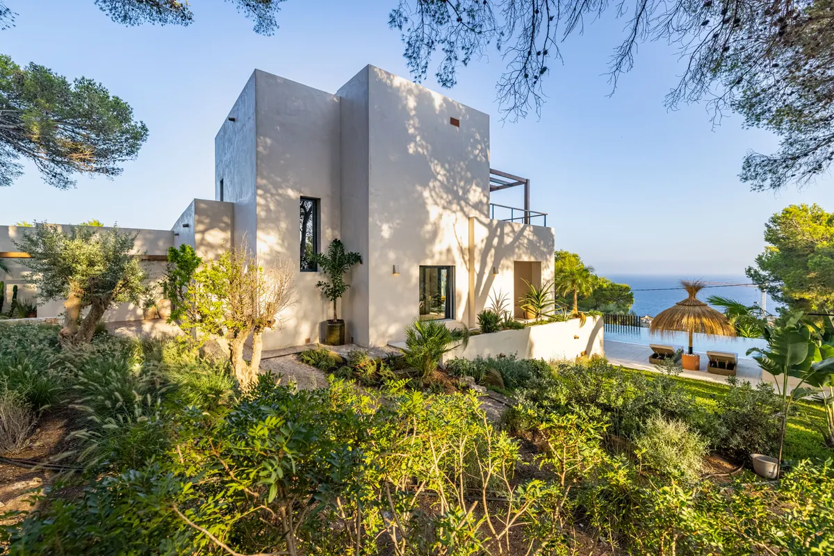 A white cubic villa among Mediterranean planting with the sea beyond
